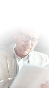 man in beige suit and black glasses reading through paperwork
