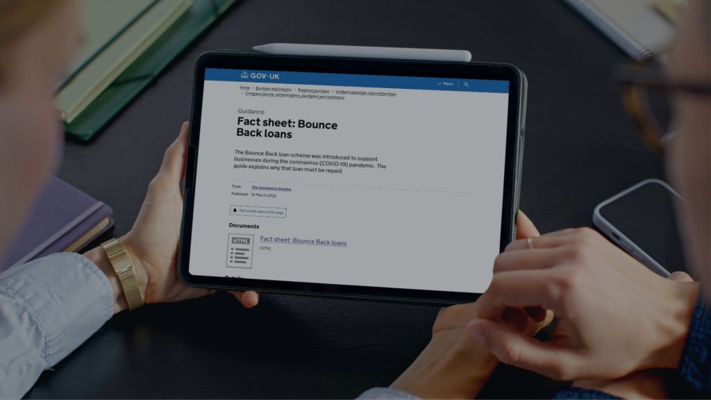 man and woman sat at a desk holding hands looking at Gov UK information on Bounce Back Loans