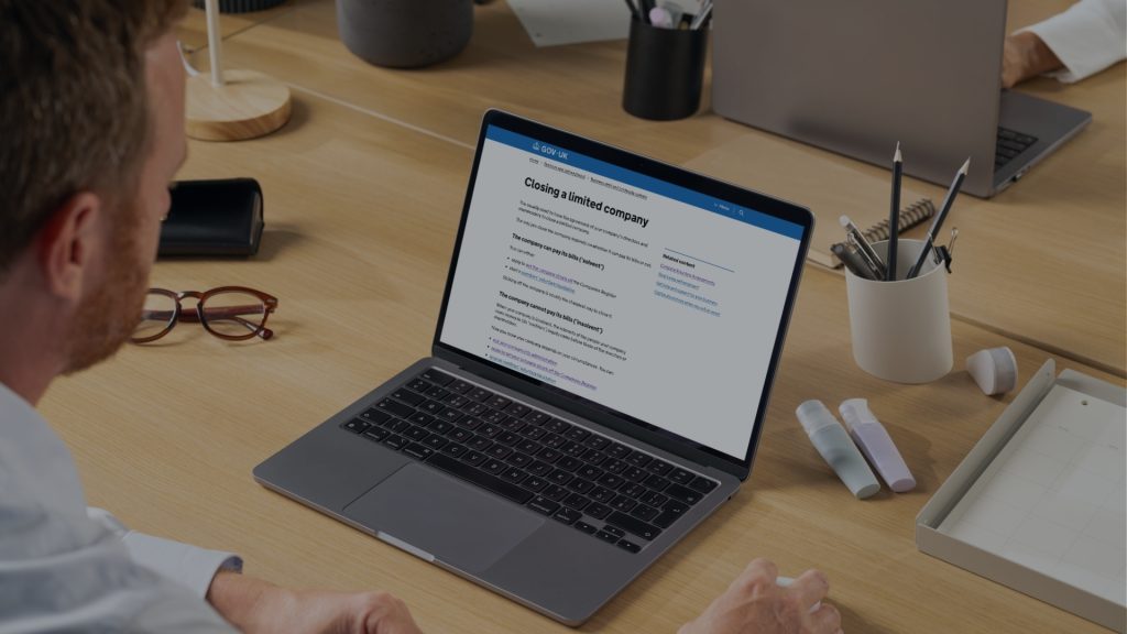 man at his desk looking at his computer on the screen is the Gov UK website for information on closing a limited company